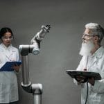 Dois cientistas trabalham com um braço robótico em um laboratório de tecnologia.