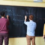 Três estudantes escrevem em um quadro sobre redução do desperdício de plástico e energia.