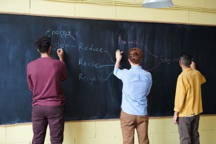Três estudantes escrevem em um quadro sobre redução do desperdício de plástico e energia.