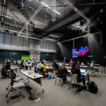 Participantes assistem a um seminário educacional em um espaço interno com telas e assentos.