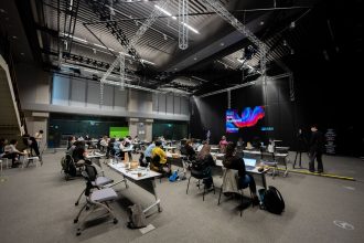 Participantes assistem a um seminário educacional em um espaço interno com telas e assentos.