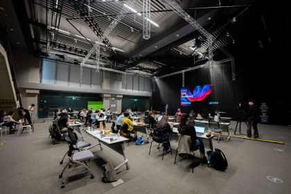 Participantes assistem a um seminário educacional em um espaço interno com telas e assentos.