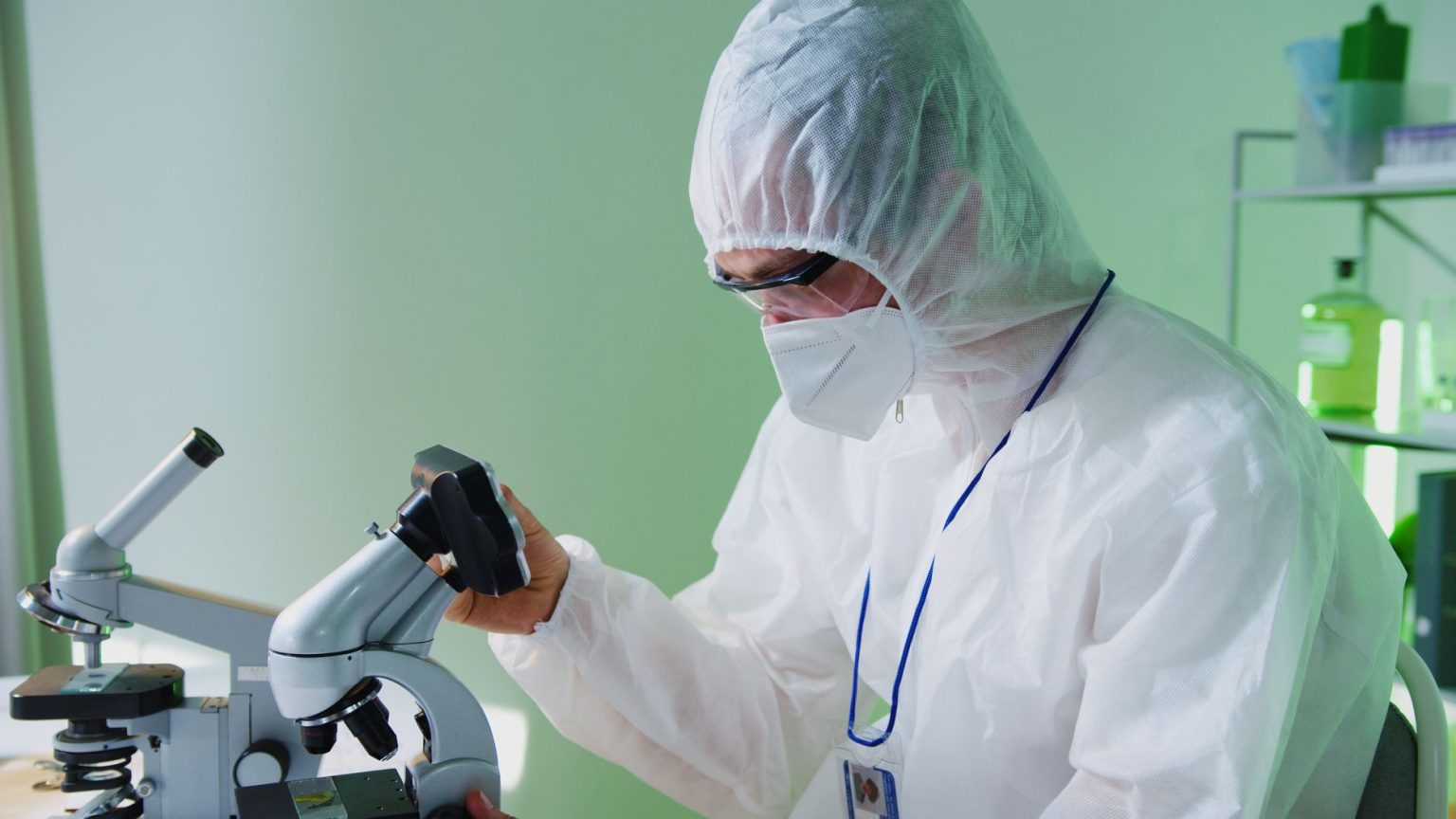 Cientista usando roupa de proteção examina amostras ao microscópio em um laboratório.