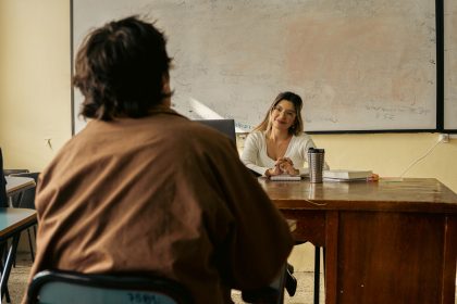 Professor conversa com estudante em uma sala de aula universitária.