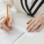 Estudante assinala respostas em uma prova de múltipla escolha sobre uma carteira escolar.