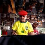 Homem idoso e menino criam juntos uma peça artística em uma oficina cultural colorida.
