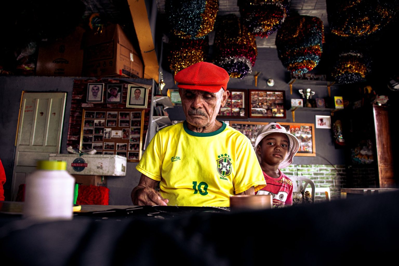 Homem idoso e menino criam juntos uma peça artística em uma oficina cultural colorida.