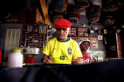 Homem idoso e menino criam juntos uma peça artística em uma oficina cultural colorida.
