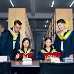 Grupo de estudantes usando becas acadêmicas estuda junto em uma biblioteca universitária.
