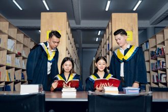 Grupo de estudantes usando becas acadêmicas estuda junto em uma biblioteca universitária.