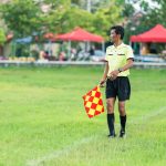 Assistente de arbitragem com bandeira em campo durante uma partida de futebol.