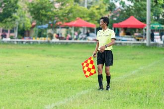 Assistente de arbitragem com bandeira em campo durante uma partida de futebol.