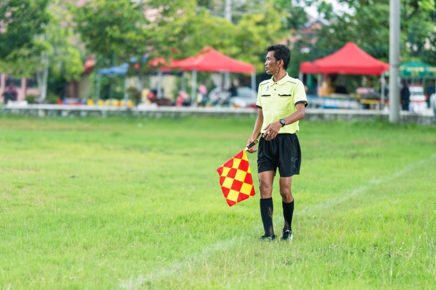 Assistente de arbitragem com bandeira em campo durante uma partida de futebol.