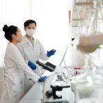 Cientistas usando equipamentos de proteção discutem experimentos em um laboratório.