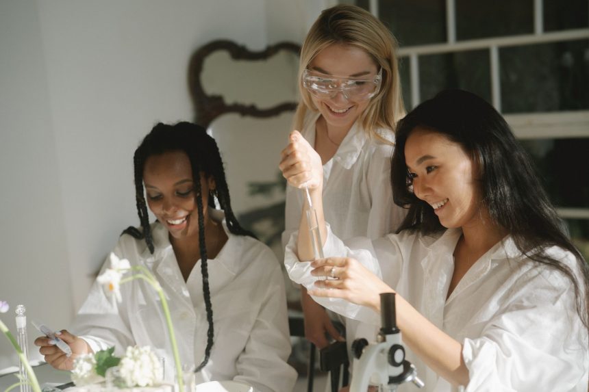 Três mulheres realizam um experimento científico com tubos de ensaio e equipamentos de laboratório.